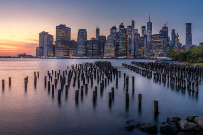 Wooden posts in sea against modern buildings in city