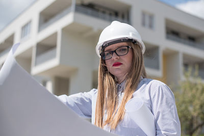 Portrait of female architect holding blueprints at construction site