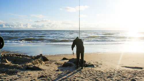 Silhouette man fishing at beach against sky