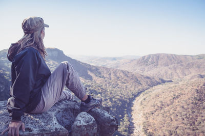 Rear view of woman sitting on rocky mountain