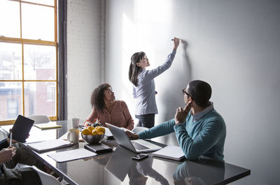 Male and female colleagues looking at businesswoman writing on whiteboard