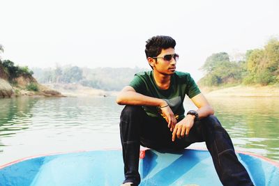 Young man sitting on sunglasses against lake