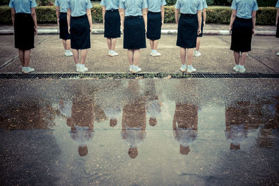 Low section rear view of women wearing uniform while standing on street by puddle