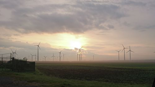 Windmills on field against sky at sunset