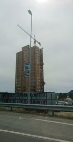 Low angle view of crane by building against sky