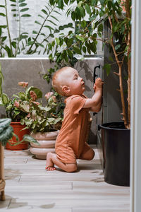 Cute toddler boy helping his mother clean domestic potted plants in bathroom 