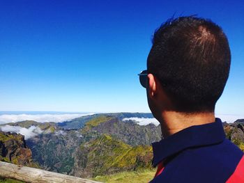 Rear view of man standing on mountain against clear blue sky