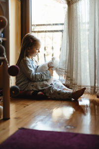 Child sitting on the floor and playing ant home. dreamy sunny mood. girl looking though the window