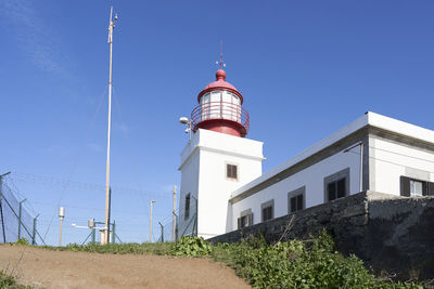 Low angle view of lighthouse amidst buildings against clear blue sky