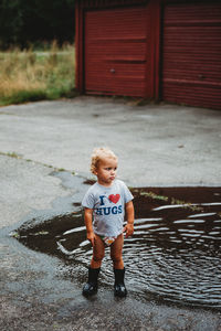 Adorable young boy pouting wearing rubber boots next to a puddle