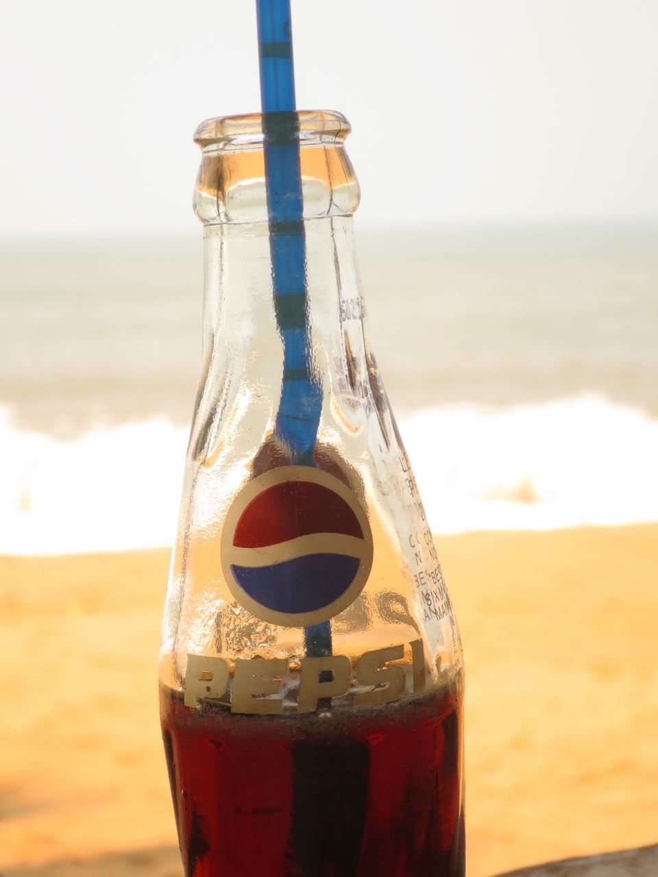 beach, sea, focus on foreground, drink, horizon over water, close-up, refreshment, sand, water, food and drink, shore, sky, selective focus, bottle, still life, no people, outdoors, drinking glass, nature, day