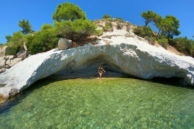 Full length of woman standing by rock formation and sea