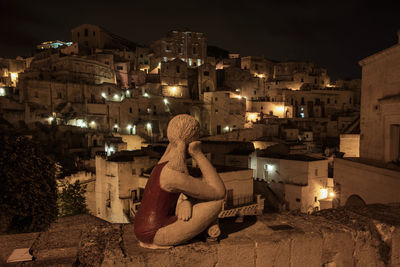 Rear view of woman sitting against illuminated buildings in city at night