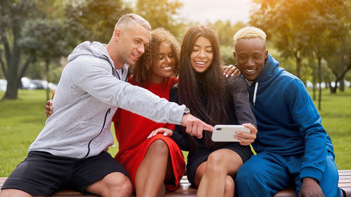 Smiling friends taking selfie while sitting at park