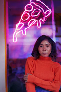 Portrait of woman standing against illuminated store