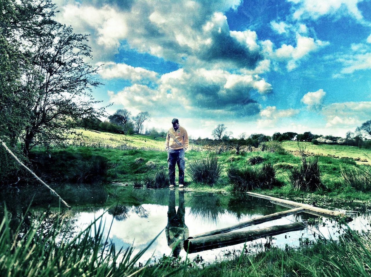 water, sky, standing, leisure activity, tranquility, lifestyles, full length, tranquil scene, reflection, lake, cloud - sky, rear view, tree, nature, grass, scenics, beauty in nature, casual clothing