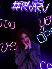 Portrait of woman standing against illuminated neon lights