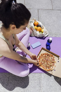 Female athlete having pizza on exercise mat during sunny day