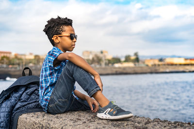 Full length of boy sitting in city against sky