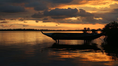 Silhouette boat in lake against orange sky