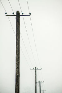 Low angle view of electricity poles against clear sky