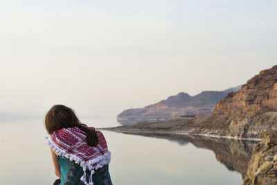 Rear view of woman by calm lake against clear sky