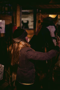 Woman adjusting horse bridle while standing outdoors at night