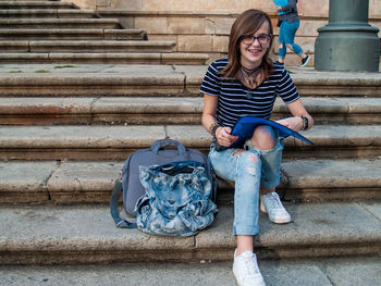 Full length portrait of woman holding folder while sitting on staircase