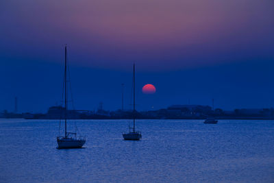 Sailboats moored on sea against sky at sunset