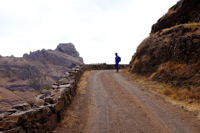 Man standing on winding road by mountain against sky