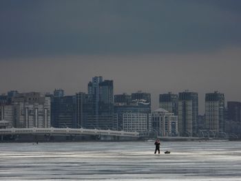 Man walking on frozen sea against buildings in city