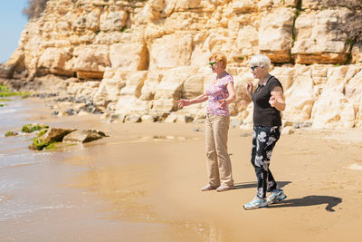 Two senior women walking along the rocky seashore and playing with the waves