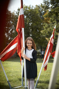 Latvian pre teen girl wearing black and white dress and standing between latvian flags masts.