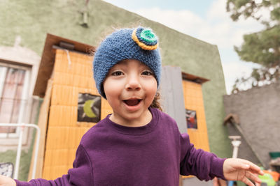 Delighted ethnic girl looking at camera with smile while standing on porch of cabin in countryside