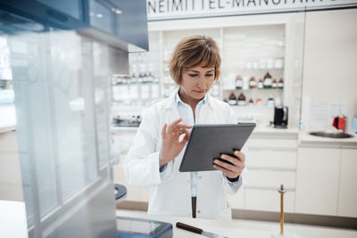 Female pharmacist using digital tablet while standing at laboratory