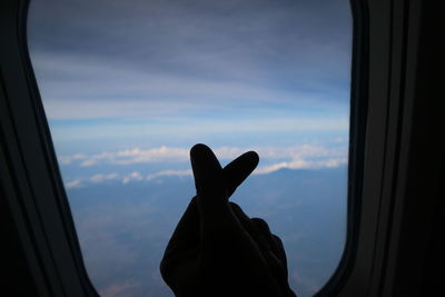 Silhouette of hand against sky seen through window