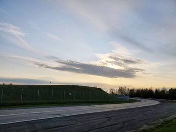 Empty road by field against sky during sunset