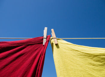 Close up of red and yellow t-shirts hanging on a washing line with wooden clothes pegs with blue sky