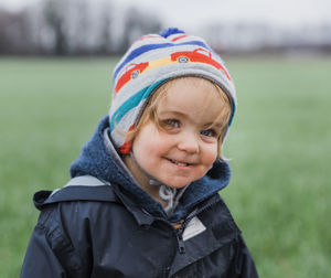 Close-up portrait of cute smiling girl in warm clothing standing on grassy field