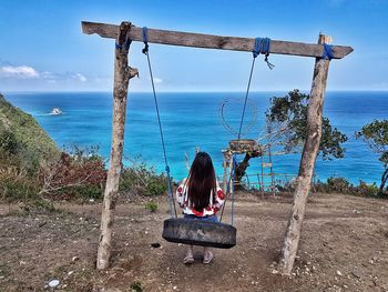 Rear view of woman looking at sea while sitting on tire swing