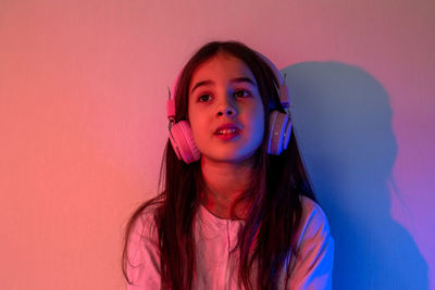 Little girl in headphones listening to music in neon light