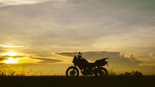 Silhouette person riding bicycle on field against sky during sunset