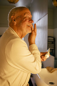 Happy senior man applying moisturizer on face in bathroom