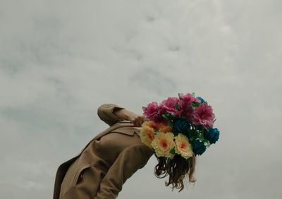 Woman face covered with bouquet against sky