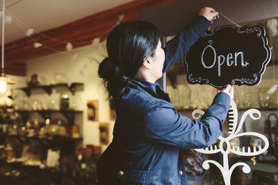 Side view of female owner hanging open sign on door of plant shop