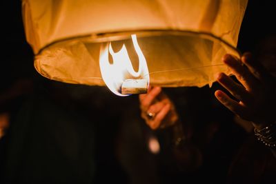 Cropped hand of woman lighting lanterns at night