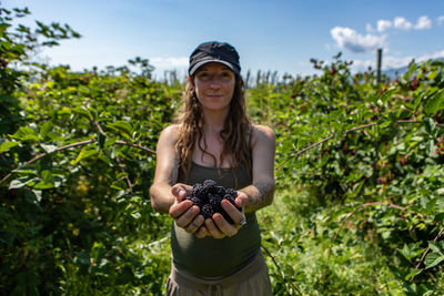 Portrait of young woman holding fruits against plants