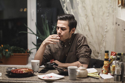 Man smoking cigarette while sitting on table at home