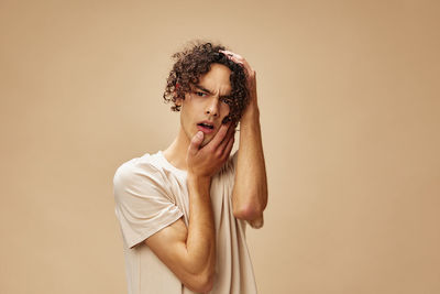 Young man gesturing against beige background