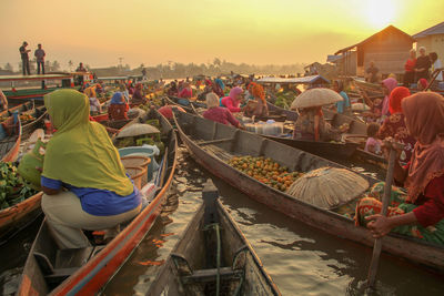 People selling food in boats on lake during sunset
